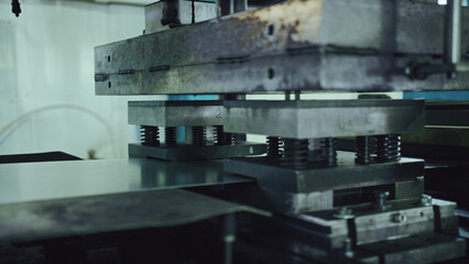 Heavy duty industrial press stamping shiny steel sheets in a factory, close up of precision metal forming and fabrication machinery used for modern automated component production