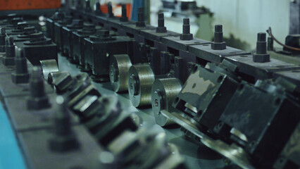 Obraz premium Industrial machinery forming a metallic sheet into a specific profile using a series of precisely aligned shaping rollers, representing modern factory automation and engineering processes