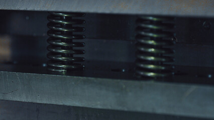 Heavy gauge metal springs compressing between two metal plates within industrial machinery. Symbolizing resistance. Pressure. And the intricacies of mechanical engineering and manufacturing processes