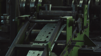 Metal strip feeds through automated punching press on factory production line, producing perforated sheet metal components in a precision metalworking operation within industrial plant