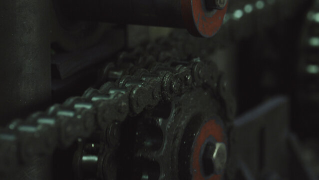 Dirty metal chain moving around a gear sprocket, suggesting mechanical power transmission and continuous movement within industrial processes and engineering