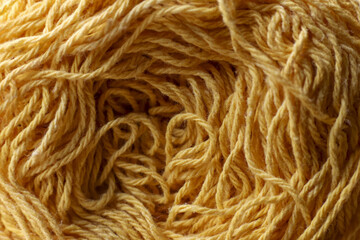 Cozy macro background texture of tangled yellow yarn. This soft wool thread close up detail for knitting, craft, or handmade projects inspires creativity and warmth