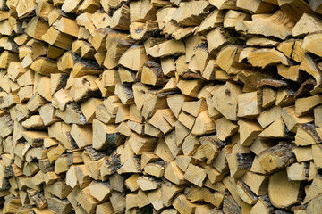 Neatly stacked split firewood, golden-brown and weathered, arranged in dense, orderly pile, ready for use. Wall of dry oak firewood stacked for winter heating fireplace or stove