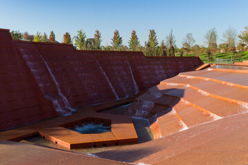 Rust-colored concrete water installation featuring multiple cascading streams flowing down. Amphitheater of water or Canyon in Public city park Krasnodar or Galitsky Park. September 2025