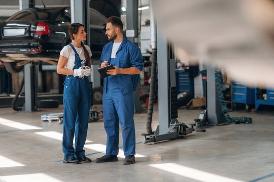 Digital tablet is in hands. Auto repair shop employees are working together. Man and woman