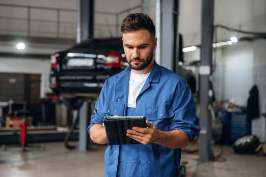 Modern digital tablet is in hands. Male mechanic is working in the car workshop
