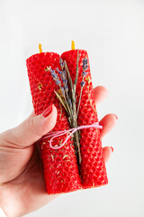 Hand holding decorative red beeswax candles with dried flowers for special occasions