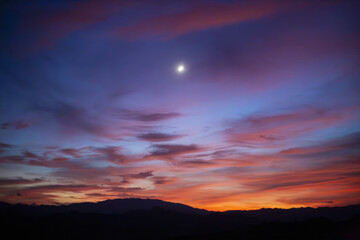 Vibrant evening sky blends deep blues, purples, fiery reds, and warm oranges, bright celestial body...