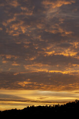 Dramatic sunset sky adorned with fiery orange and golden clouds. Peaceful evening scene unfolds above dark landscape silhouette, evoking feelings of serenity and wonder