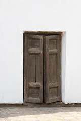 Historical wooden dark double door. Ajar double wooden door in a white stone wall