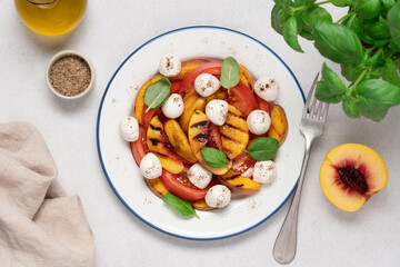 Top view of Caprese salad with grilled peach, fresh tomatoes, mozzarella, and basil on a light background. Summer Italian cuisine concept