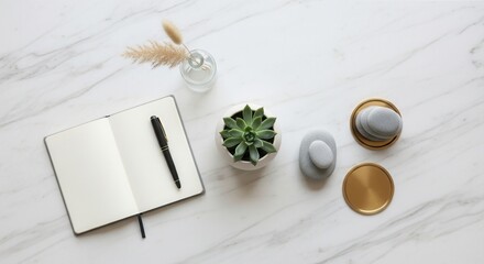 Flat lay of an open notebook with a pen a succulent plant a vase with dried grass smooth grey stones and round brass coasters on a white marble surface