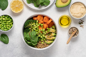 White Bowl with with Healthy Quinoa Salad, Edamame Beans, Broccoli, Carrot, Lettuce Leaves and Avocado Surrounded by Ingredients  on Light Background, Clean Eating Concept