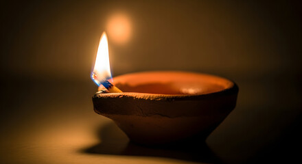 Close up of a diya lamp with a bright flame in a dimly lit environment