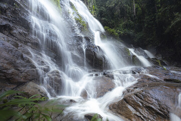 Fototapeta premium Magnificent waterfall cascade over wet rock, showcasing smooth flow and dynamic motion of water. green lush forest environment evokes serene, tranquil, and peaceful feeling