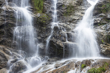 Fototapeta premium Cascading waterfall flowing over rugged rocks, evoking powerful, serene, and refreshing natural beauty. White water descends gracefully, creating tranquil environment and peaceful sound