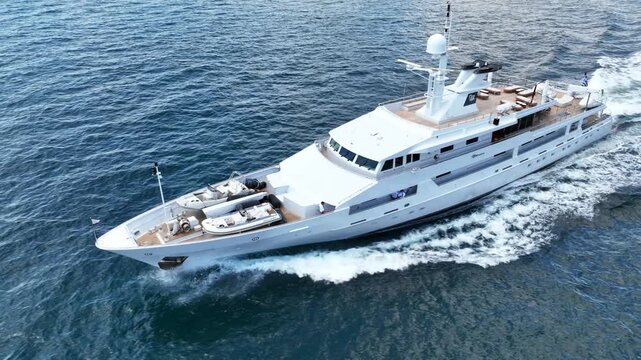 Aerial drone cinematic tracking video of luxury yacht with wooden deck cruising deep blue Aegean Sea, Mykonos island, Cyclades, Greece