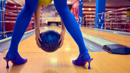 Woman in blue leggings and heels preparing to throw heavy bowling ball. Concept of surreal fashion mix, female empowerment, playful provocation, sport reinterpretation and bold creative imagery.