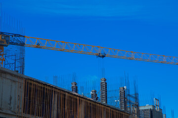 Close-up of the construction site of the building, on the top floor there are fittings, formwork and next to it a crane against the background of a blue sky. High quality photo