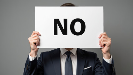 Businessman holding sign with word NO in bold letters, expressing clear refusal or disagreement. background is neutral and professional
