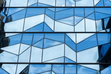 Contemporary building facade with geometric blue glass panels with angular shapes and reflective...