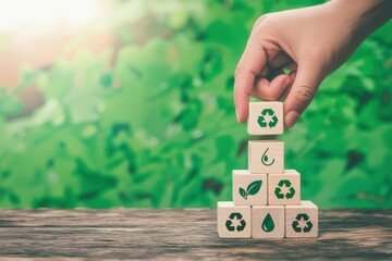 Fototapeta premium Hand building a pyramid of wooden blocks with eco-friendly symbols on a wooden surface against a green blurred background