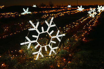 Bright illuminated snowflake light with glowing, shining garlands in background, creating magical winter holiday atmosphere. Christmas and New Year light installations, street decor