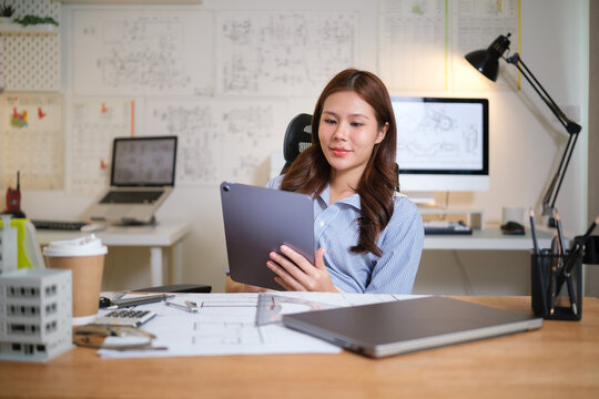 Female architect using a digital tablet to review construction plans in a modern design studio.
