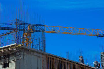 Close-up of the upper floor of the building under construction, you can see the reinforcement, mesh and formwork, next to the crane against the blue sky. Concept of construction, erection of buildings