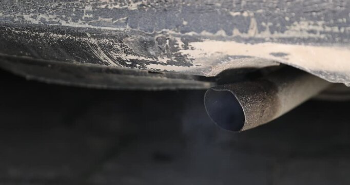blue smoke from the muffler of an old car with an inoperable or not installed filter for cleaning exhaust gases, an old pipe in the car for releasing exhaust gases from the car engine