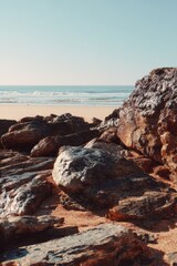 Coastal Rocks Dominate Beach Scene Under Clear Blue Sky, Serene Landscape.