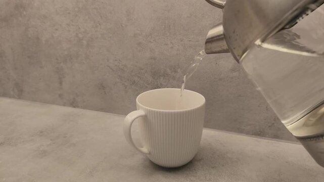 Hand pours hot water into a white ribbed cup on a smooth gray surface, capturing the fluid motion and anticipation of a warm beverage being prepared