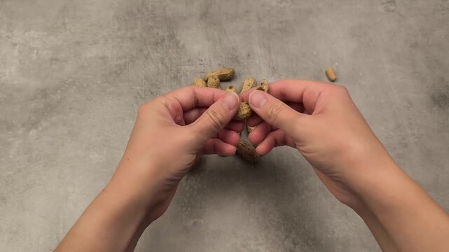 Hands skillfully peeling peanuts in a continuous motion sequence, showcasing the detailed process of removing shells from the nuts on a textured surface