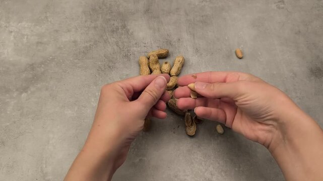 Hands skillfully shelling peanuts in a continuous motion, showcasing the process of separating shells from nuts on a textured surface