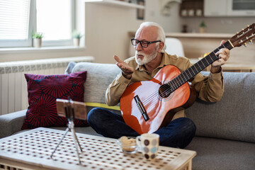 An older man is filming a music video and sending kisses. Bearded senior man playing on guitar...