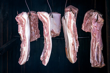 Fresh pork meat hanging on metal hooks in a traditional smokehouse. Concept of meat industry, food production, and traditional processing.