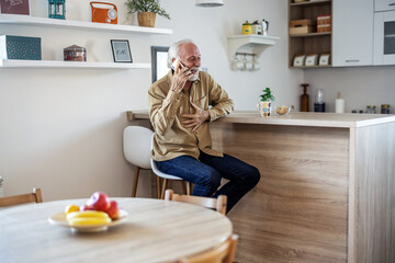 Mature man using phone in kitchen at home. Happy male drinking coffee, using smartphone and 5g wifi technology connection in house.