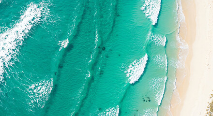 Top-down aerial view of vibrant turquoise ocean waves breaking and creating white foam lines on a strip of pale beach sand