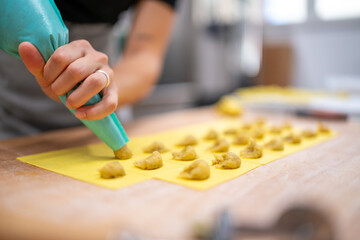 Close up shot of a person's hands expertly piping small dollops of dough onto a bright yellow pasta sheet preparing to make homemade ravioli in a bright airy kitchen setting