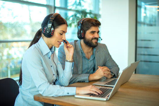 Female and male call center agents talking to clients on laptops with headsets in office
