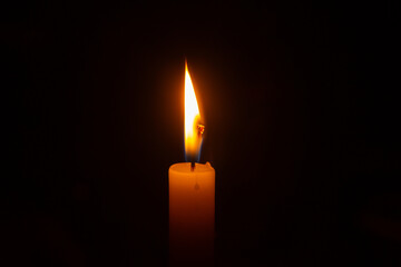 Close up na chama acesa de uma vela com fundo escuro.