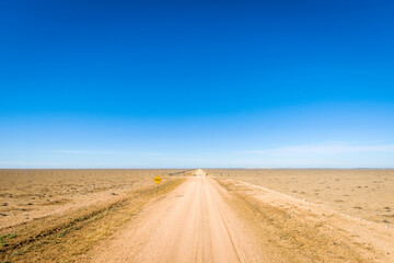 Straight dirt road through flat arid plains under clear blue sky