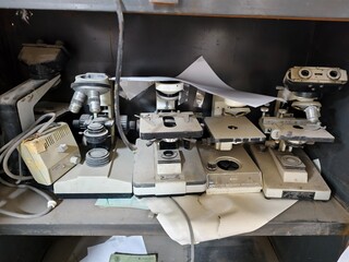 Basrah, Iraq - October 1, 2025: Close-up of old, dusty microscopes with tangled wires on shelves.

