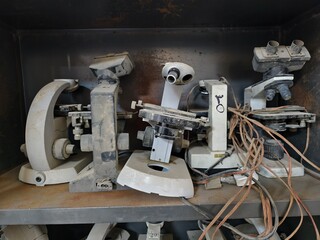 Basrah, Iraq - October 1, 2025: Close-up of old, dusty microscopes with tangled wires on shelves.

