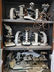 Basrah, Iraq - October 1, 2025: Close-up of old, dusty microscopes with tangled wires on shelves.

