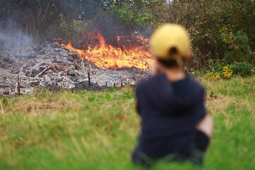 The boy sits and looks at the fire in forest