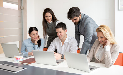 Obraz premium Group of business people gathered around young manager working on laptop developing strategy