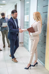 Businessman and businesswoman shaking hands in hallway after spontaneous meeting