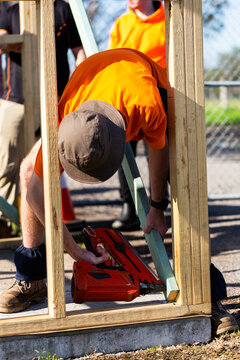 Tradie apprentice using nail gun to secure temporary support structure on building frame