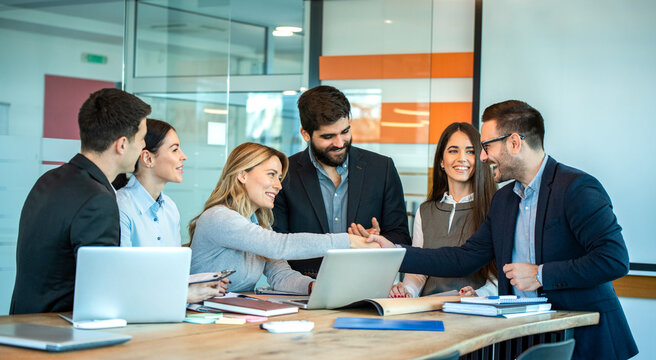 Professional business team celebrating successful project completion with handshake and smiles